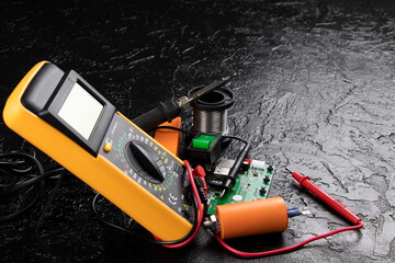 Digital multi-meter with probes on a black stone background. Multitester and microcircuit. Voltage...