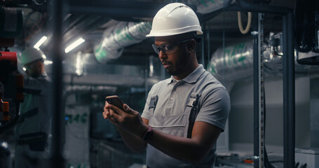 African American engineer uses mobile phone to inspect pipeline system on plant. Professional male...
