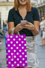 Closeup view of woman hand shopping with a smart phone and carrying bags. Shopaholic