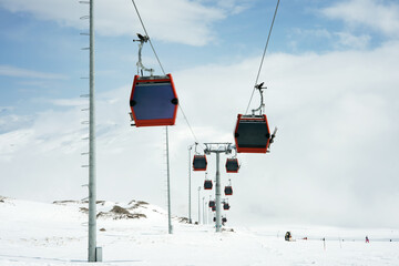 Cable car or ski lift cabins moving far away against the background of snow-covered mountains and blue sky in the mountain ski resort Perspective  Winter, Vacation. Extreme sport.  Travel content