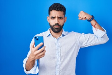 Hispanic man with beard using smartphone typing message strong person showing arm muscle, confident and proud of power