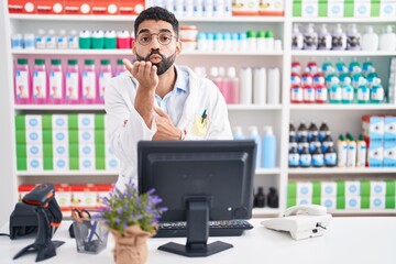 Hispanic man with beard working at pharmacy drugstore looking at the camera blowing a kiss with...
