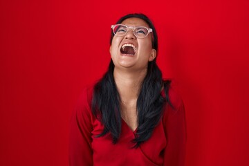 Asian young woman standing over red background angry and mad screaming frustrated and furious,...
