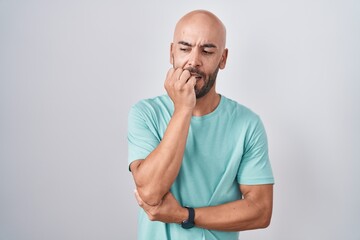 Middle age bald man standing over white background looking stressed and nervous with hands on mouth...