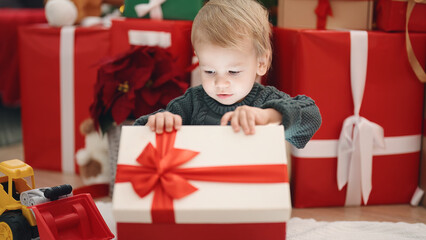 Fototapeta na wymiar Adorable blond toddler unpacking christmas gift sitting on floor at home