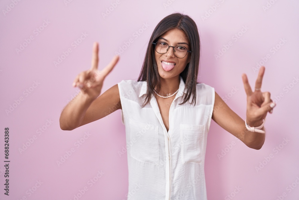 Wall mural brunette young woman standing over pink background wearing glasses smiling with tongue out showing f