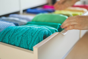 Women's hands take bright rainbow clothes from a wardrobe drawer. The concept of order and storage