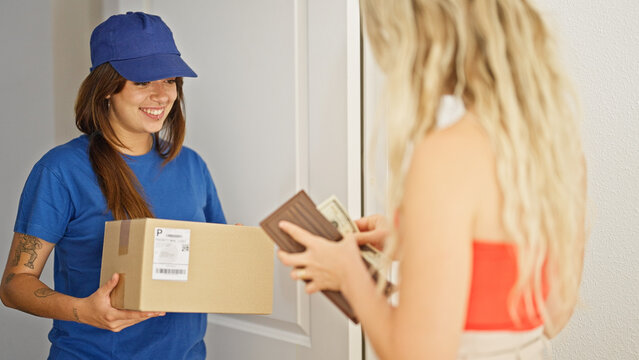 Young beautiful hispanic woman delivery woman giving package to client paying dollars at home