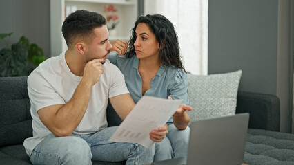 Man and woman couple using laptop reading document looking upset at home