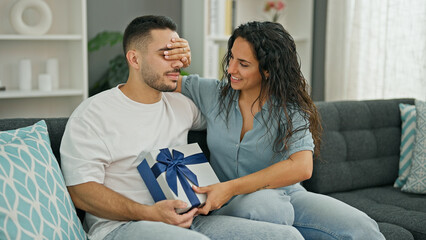 Obraz na płótnie Canvas Man and woman couple surprised with gift covering eyes with hand at home