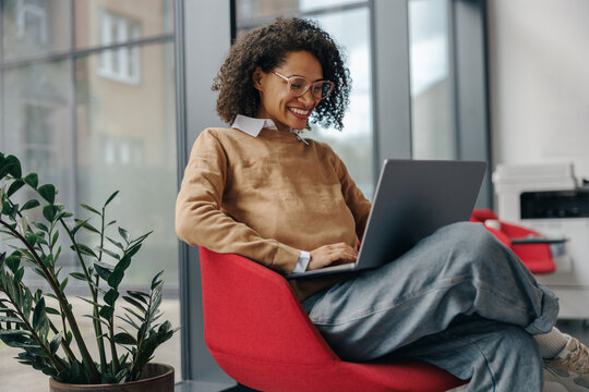Pretty female freelancer working on laptop while sitting on modern coworking background