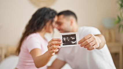 Man and woman couple sitting on bed holding baby ultrasound at bedroom
