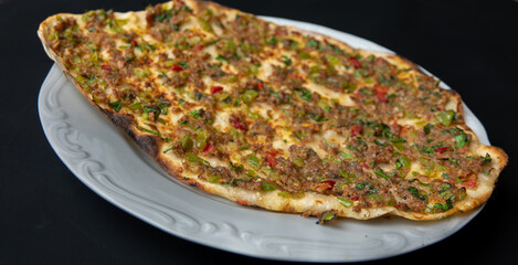 Traditional delicious Turkish foods lahmacun with mince lamb meat on white plate isolated on black background