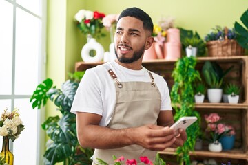Young latin man florist smiling confident using smartphone at flower shop