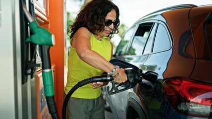 Middle age hispanic woman putting gas in the car at gas station