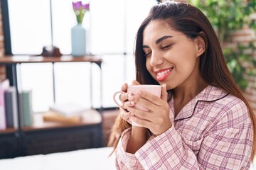 Young beautiful arab woman drinking cup of coffee sitting on bed at bedroom