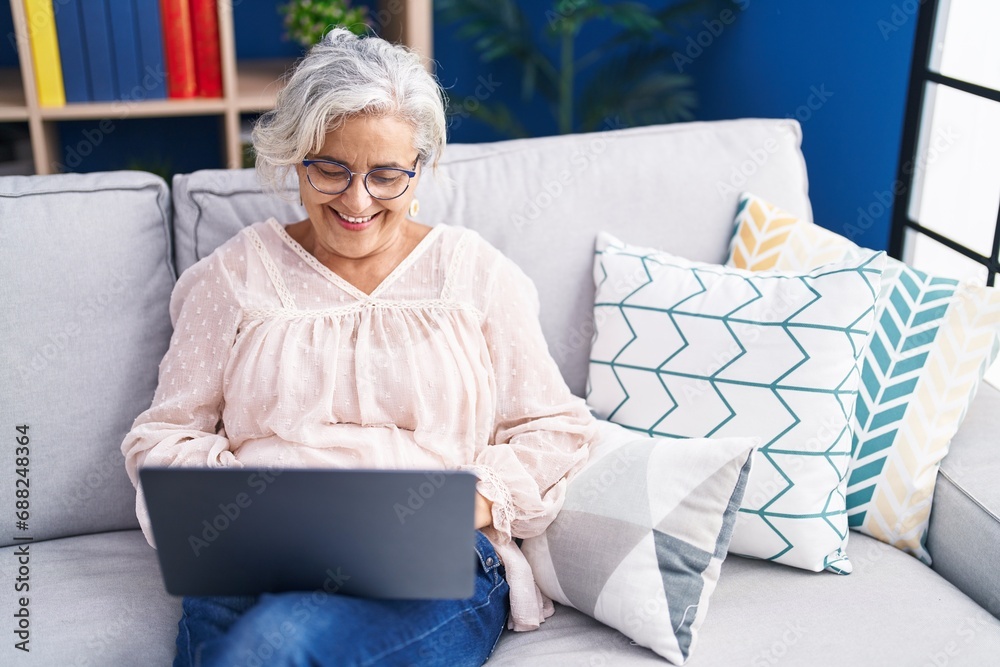 Canvas Prints Middle age grey-haired woman using laptop sitting on sofa at home - Canvas Prints