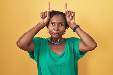 African woman with dreadlocks standing over yellow background doing funny gesture with finger over...