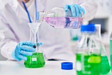 Young caucasian man scientist pouring liquid on test tube at laboratory