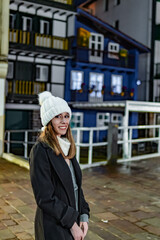Fototapeta premium Caucasian girl in white winter attire: dusk, colorful village backdrop, charming lights.