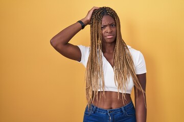African american woman with braided hair standing over yellow background confuse and wondering...