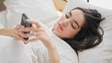 Young beautiful hispanic woman using smartphone lying on bed at bedroom
