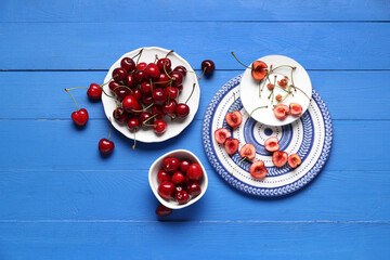 Plates and bowl of sweet cherries on blue wooden background