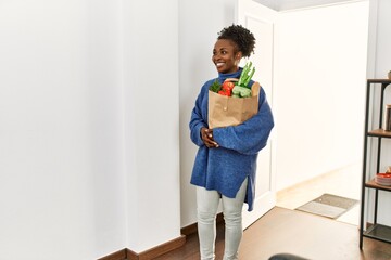 African american woman holding groceries bag walking through the door at home