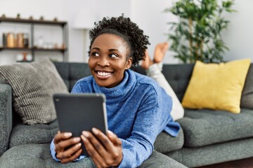 African american woman using touchpad lying on sofa at home - Powered by Adobe