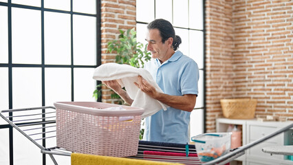 Middle age man holding clothes of basket at laundry room