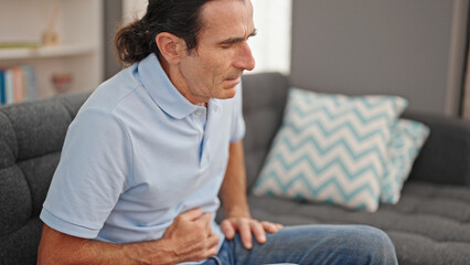Fototapeta premium Middle age man suffering for stomach ache sitting on sofa at home