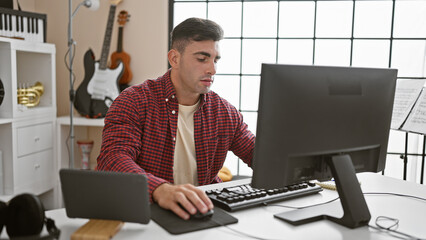 Relaxed young hispanic musician perfecting his art, tuning his soulâ€™s melody using computer...