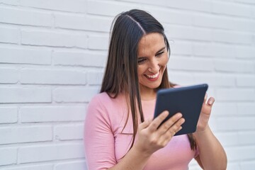 Young beautiful hispanic woman smiling confident using touchpad over isolated white brick background