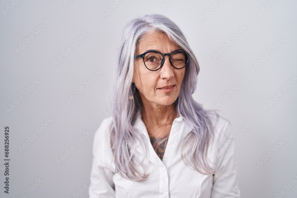 Wall mural Middle age woman with tattoos wearing glasses standing over white background winking looking at the camera with sexy expression, cheerful and happy face.