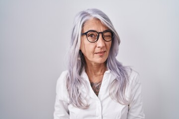Middle age woman with tattoos wearing glasses standing over white background winking looking at the...