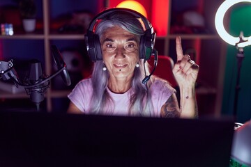 Middle age woman with tattoos playing video games wearing headphones smiling with an idea or...
