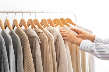 Women's hands choose neutral clothes from a hanger. White, beige and gray jersey.