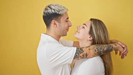 Beautiful couple smiling confident hugging and looking each other over isolated yellow background