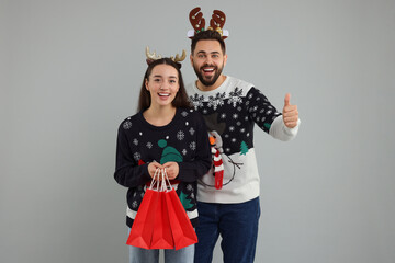 Happy young couple in Christmas sweaters and reindeer headbands with shopping bags on grey...