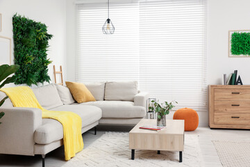 Green artificial plant wall panel and comfortable furniture in cozy living room. Interior design