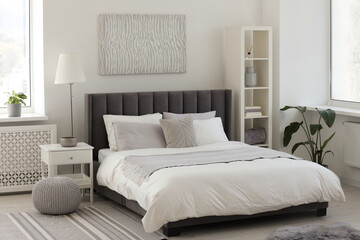 Stylish light bedroom interior with large comfortable bed, shelving unit and bedside table