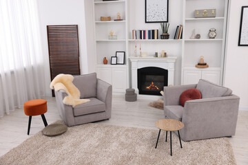 Comfortable armchairs, fireplace and shelves in living room. Interior design