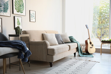 Stylish living room interior with comfortable sofa, plaid and guitar
