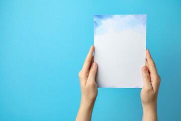 Woman holding blank invitation card on light blue background, closeup. Space for text