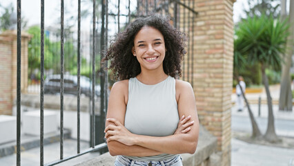 Joyful young hispanic woman flaunting her beautiful curly hair and infectious smile, standing...