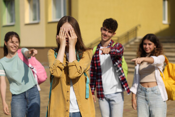 Teen problems. Group of students pointing at upset girl outdoors, selective focus