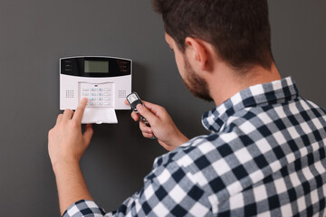 Man checking home security alarm system with key fob near gray wall