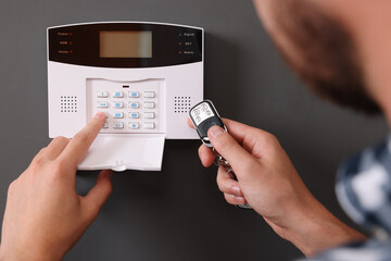 Man checking home security alarm system with key fob near gray wall, closeup