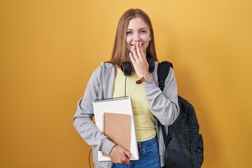 Young caucasian woman wearing student backpack and holding books laughing and embarrassed giggle...
