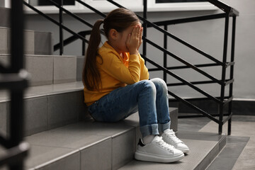 Child abuse. Upset little girl sitting on stairs indoors